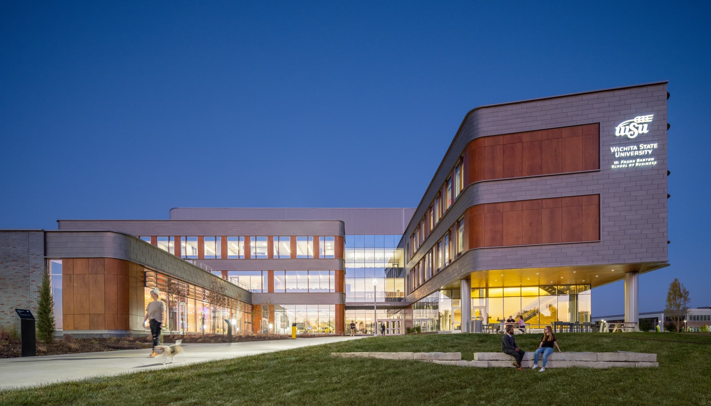 The Barton School of Business at Wichita State University lit at dusk, with terracotta panels wrapping a glazed curtain wall